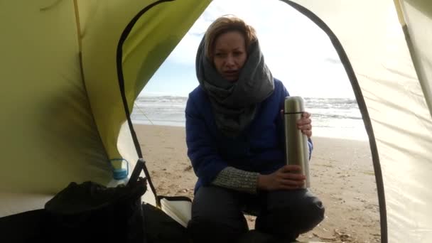 海边的沙滩上露营的帐篷。4k 慢动作一个女人坐在帐篷旁边的热水瓶 — 图库视频影像