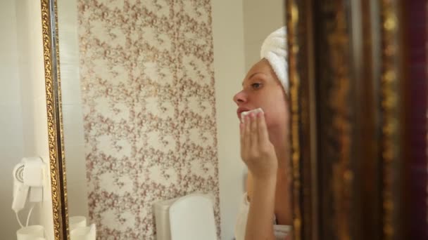 Mujer aplicando mascarilla hidratante para la piel en la cara mirando en espejo en el baño. 4k, cámara lenta — Vídeo de stock