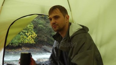 bir turist çadır 4 k. görünümünden bir dağ nehir üzerinde. adam bir kupa termos içinde çay dökülen ve dağ nehir görünüyor.
