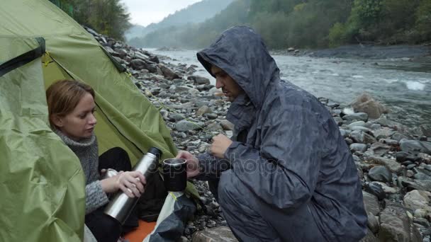 4 k. uitzicht vanaf een toeristische tent aan een rivier berg. de man met het meisje giet thee in de thermos fles en kijkt naar de rivier van de berg. — Stockvideo