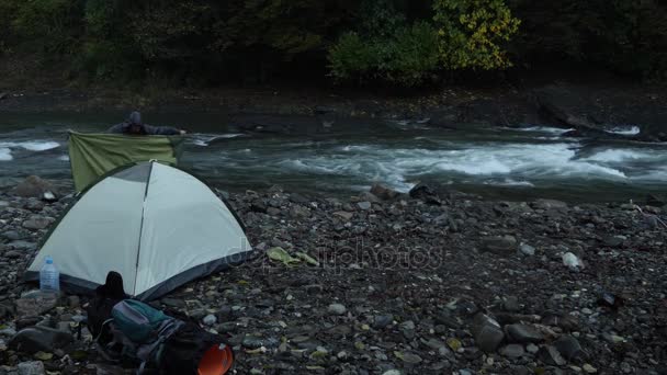 4k. un gars près d'une tente touristique sur la rive d'une rivière de montagne . — Video