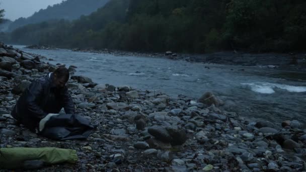 4 k. de man zet een toeristische tent aan de oever van een rivier berg. — Stockvideo