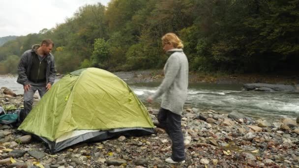 4k. un ragazzo e una ragazza vicino a una tenda turistica sulla riva di un fiume di montagna . — Video Stock