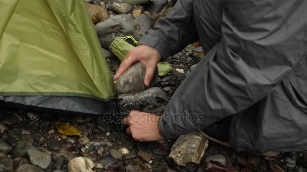 4k. el tipo pone una tienda de campaña turística en la orilla de un río de montaña . — Vídeos de Stock