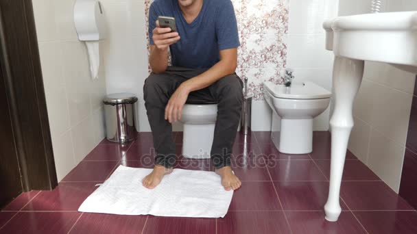 Man sitting on a toilet and looking in the cell phone. 4k, slow motion — Stock Video