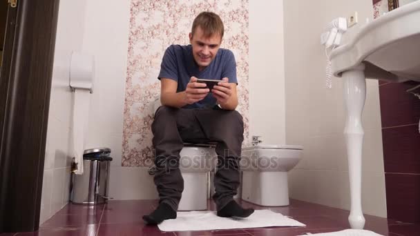 Homme assis sur les toilettes et regardant dans le téléphone portable. 4k, au ralenti — Video