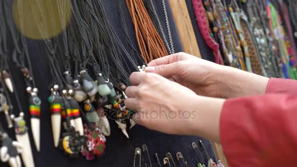 Красивые украшения хиппи. Женщина смотрит сквозь украшения в витрине уличного рынка. 4k, slow motion — стоковое видео