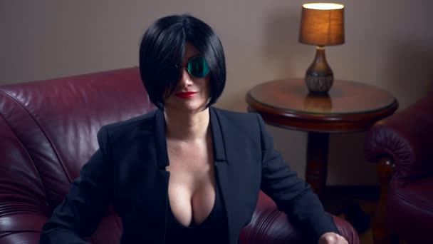 Brune chaude en lunettes de soleil rondes, assise dans un fauteuil et montre un drap avec l'inscription sexe. 4k, mouvements lents — Video