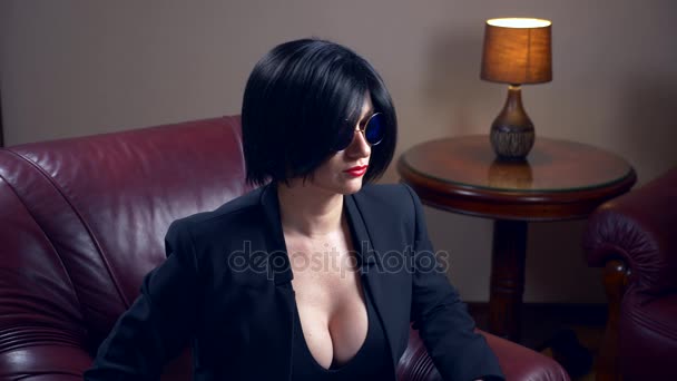 Morena caliente en gafas de sol redondas, se sienta en una silla y muestra una sábana con la inscripción sexo y amor. 4k, cámara lenta — Vídeo de stock