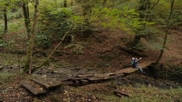 Мужчина-турист больше ходит по самодельному переходу через горную реку в лесу. 4k, slow motion — стоковое видео