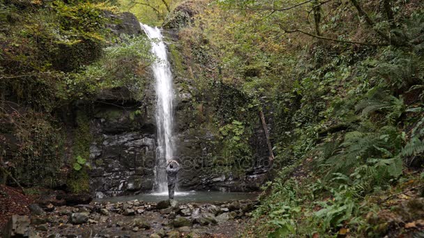 Mochileiro homem feliz desfrutando de cachoeira tropical incrível.Viagem Estilo de vida e férias conceito de sucesso na natureza selvagem na montanha de fundo. 4k, câmera lenta — Vídeo de Stock