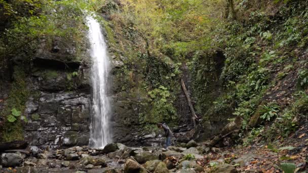 Lycklig man backpacker njuter av fantastiska tropiska vattenfall. Resa livsstil och framgång konceptet semestrar i den vilda naturen på bakgrunden berget. 4k, Slowmotion — Stockvideo