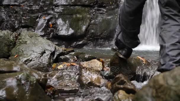 4k, slowmotion. en turist man är att plocka upp vatten från en sjö vid foten av ett berg bredvid ett vattenfall. — Stockvideo