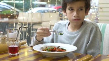 Çocuk bir çatal ile sebze ve et ile sıcak bir salata yiyor. Restoran, arka plan bulanık. 4k