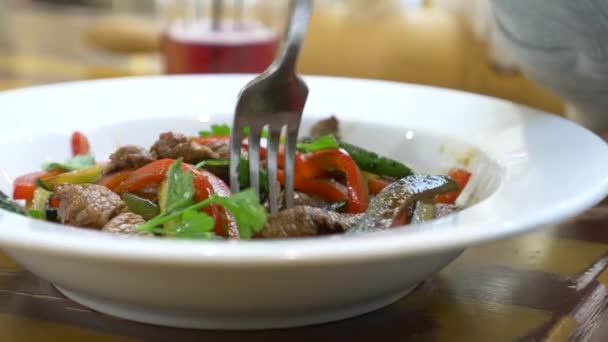 O menino come uma salada quente com carne e legumes com um garfo. restaurante, fundo borrado. 4k — Vídeo de Stock