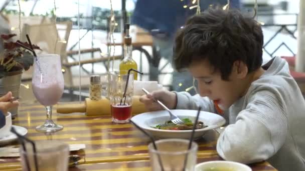 The boy eats a warm salad with meat and vegetables with a fork. restaurant, blurred background. 4k — Stock Video