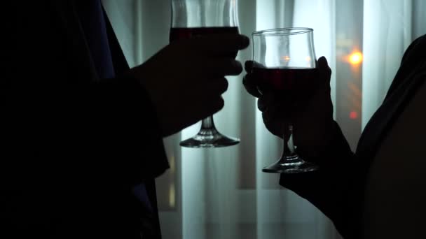Jeune femme et homme buvant du vin debout près de la fenêtre d'une maison la nuit. Panorama des fenêtres, vue sur la ville, veilleuses. 4k — Video