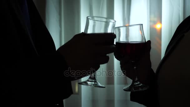 Mujer joven y hombre bebiendo vino de pie junto a la ventana de una casa por la noche. Ventana panorámica, vista de la ciudad, luces nocturnas. 4k — Vídeo de stock