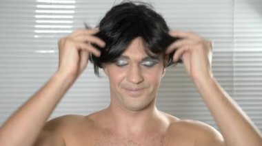 Travesti makyaj. genç bir adam kendine bir transseksüel mencap hazırlar. 4k, ağır çekim. o peruk üzerinde koyar ve sosyal ağ kendi Smartphone'da koyar
