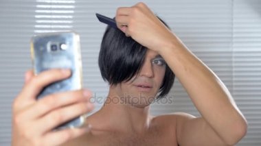 Travesti makyaj. genç bir adam kendine bir transseksüel mencap hazırlar. 4k, ağır çekim. o peruk üzerinde koyar ve sosyal ağ kendi Smartphone'da koyar