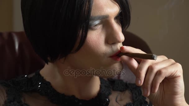 Un jeune homme à l'image d'un transsexuel fumant séduisamment un cigare au crépuscule et libérant de la fumée dans la caméra. 4k, au ralenti — Video