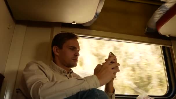 Una persona utiliza un teléfono inteligente en un compartimento de un tren de pasajeros. 4k — Vídeo de stock