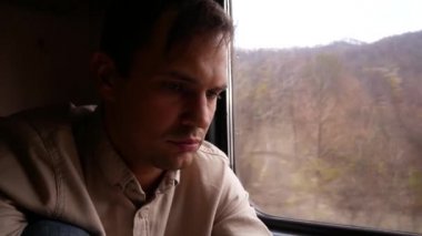 Şehvetli dudakları olan genç bir adam tren penceresinin arka plan karşı bir şey düşünüyor. 4 k. manzara, hareket, doğa, ağaç ve orman bir trenin penceresinden görünümü.