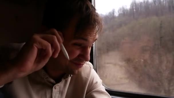 Młody człowiek z zmysłowe usta myśli, coś na tle okna pociągu. 4 k. krajobraz, widok drzewa i Las z okna pociągu w ruchu, natura. — Wideo stockowe
