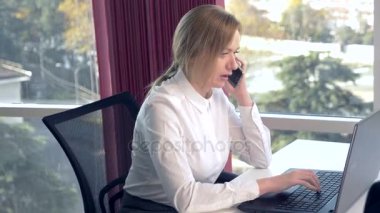 iş kadını bir panoramik pencere, güneşli bir gün, dizüstü bilgisayar, tablet, modern bir ofiste bir durumda bir cep telefonu kullanın. 4k, ağır çekim