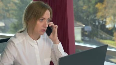 iş kadını bir panoramik pencere, güneşli bir gün, dizüstü bilgisayar, tablet, modern bir ofiste bir durumda bir cep telefonu kullanın. 4k, ağır çekim