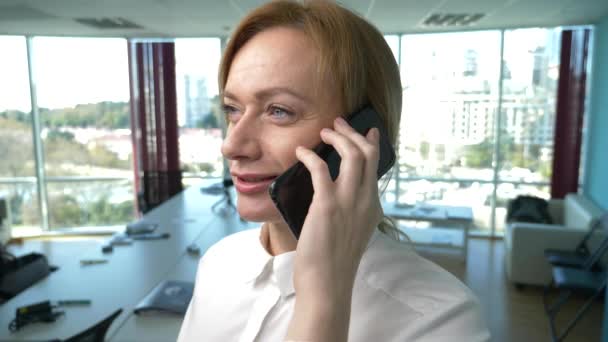 Γυναίκα των επιχειρήσεων σε ένα σύγχρονο γραφείο με ένα πανοραμικό παράθυρο, ηλιόλουστη μέρα, laptop, tablet, χρησιμοποιήστε ένα κινητό τηλέφωνο σε μια κατάσταση. 4k, αργή κίνηση — Αρχείο Βίντεο