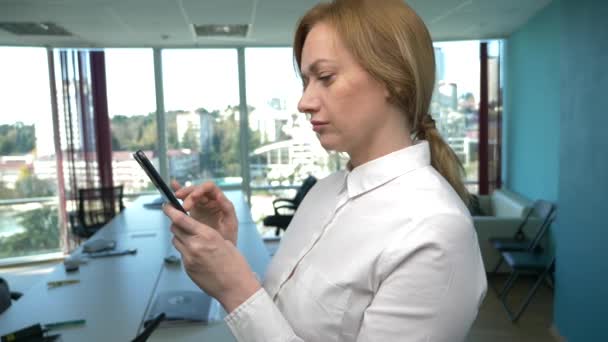 Mulher de negócios em um escritório moderno com uma janela panorâmica, dia ensolarado, laptop, tablet, use um telefone celular em uma situação. 4k, câmera lenta — Vídeo de Stock