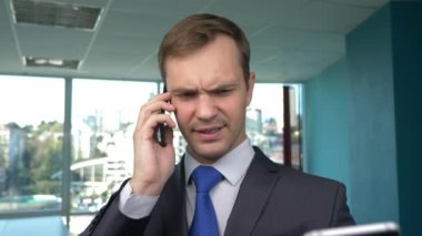 iş adamı panoramik pencereli, modern bir ofiste güneşli bir gün, bir cep telefonu bir durumda kullanım. 4k, ağır çekim