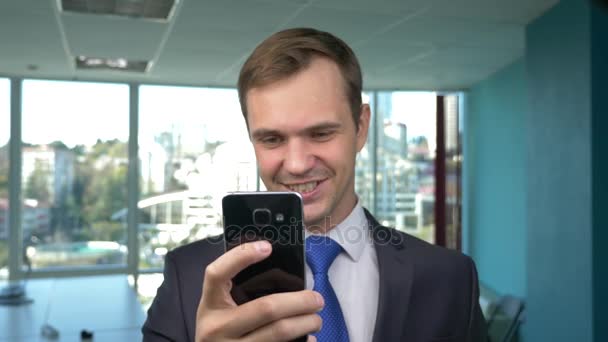 Homem de negócios em um escritório moderno com uma janela panorâmica, dia ensolarado, use um telefone celular em uma situação. 4k, câmera lenta — Vídeo de Stock