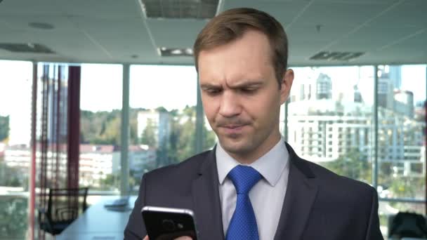 Homem de negócios em um escritório moderno com uma janela panorâmica, dia ensolarado, use um telefone celular em uma situação. 4k, câmera lenta — Vídeo de Stock