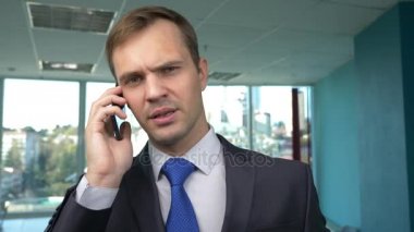 iş adamı panoramik pencereli, modern bir ofiste güneşli bir gün, bir cep telefonu bir durumda kullanım. 4k, ağır çekim