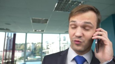 iş adamı panoramik pencereli, modern bir ofiste güneşli bir gün, bir cep telefonu bir durumda kullanım. 4k, ağır çekim