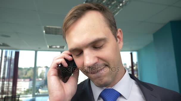 Άνθρωπος των επιχειρήσεων σε ένα σύγχρονο γραφείο με ένα πανοραμικό παράθυρο, ηλιόλουστη μέρα, χρησιμοποιήστε ένα κινητό τηλέφωνο σε μια κατάσταση. 4k, αργή κίνηση — Αρχείο Βίντεο