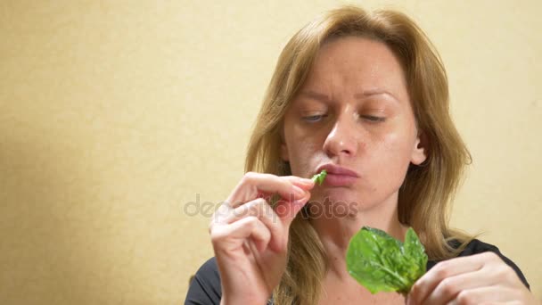 Bella donna bionda che mangia un foglio di spinaci. Una donna si mette una verdura fresca verde in bocca. Il concetto di cibo vegetariano o sano. 4k, rallentatore — Video Stock