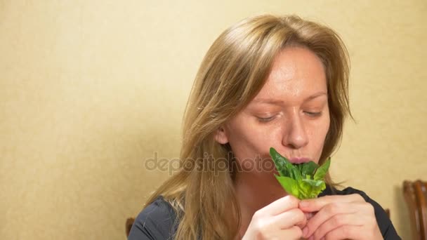 Bella donna bionda che mangia un foglio di spinaci. Una donna si mette una verdura fresca verde in bocca. Il concetto di cibo vegetariano o sano. 4k, rallentatore — Video Stock