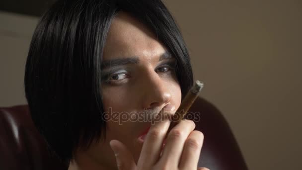 Genç bir adam bir transeksüel suretinde seductively duman alacakaranlıkta bir puro sigara ve serbest kameraya. 4k, ağır çekim — Stok video
