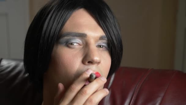 Молодой человек в образе транссексуала, соблазнительно курящего сигару в сумерках и выпускающего дым в камеру. 4k, slow motion — стоковое видео