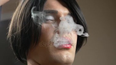 genç bir adam bir transeksüel suretinde seductively duman alacakaranlıkta bir puro sigara ve serbest kameraya. 4k, ağır çekim