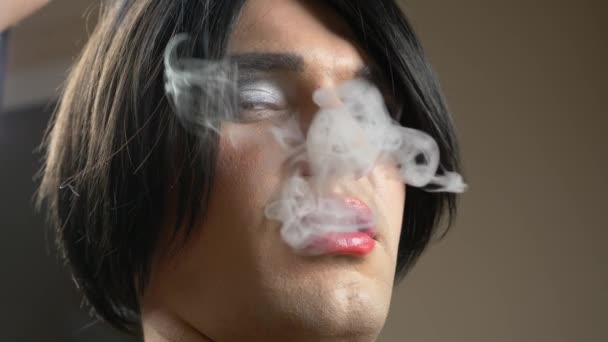 一个年轻男子在一个变性人的形象诱惑抽雪茄在黄昏和释放烟雾进入相机。4k、慢动作 — 图库视频影像