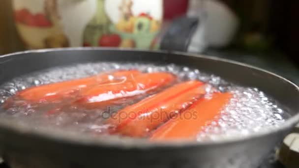 Salsichas não cozidas são fervidas em água em um fogão a gás. 4k, câmera lenta — Vídeo de Stock