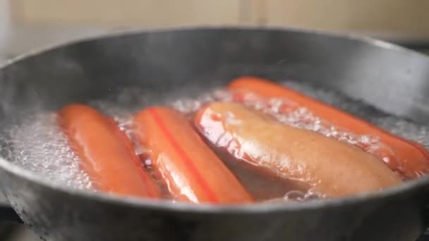 Salsichas não cozidas são fervidas em água em um fogão a gás. 4k, câmera lenta — Vídeo de Stock