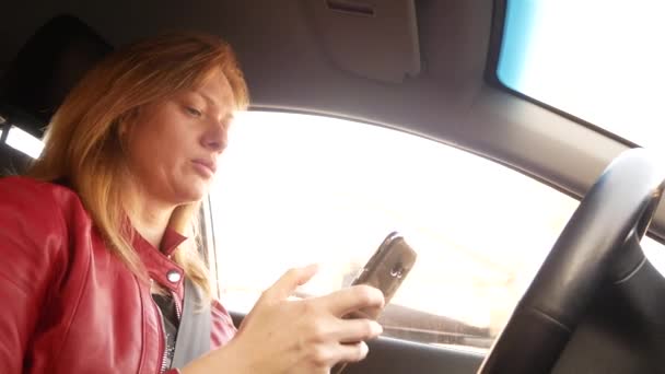 Женщина пишет за рулём. Смартфон в машине. 4k — стоковое видео
