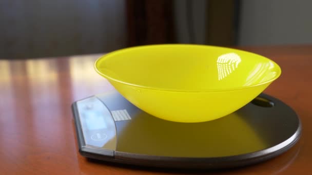 Quelqu'un mesure un morceau de farine d'avoine, sur une balance électronique dans la cuisine. verser la croupe dans un bol rond profond, debout sur une plate-forme de pesage plate. 4k, ralenti, tir de poupée — Video