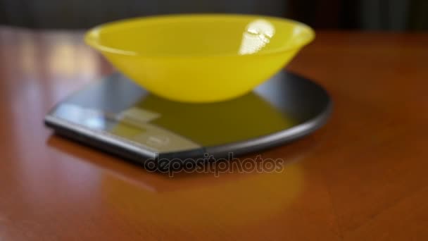 Quelqu'un mesure un morceau de riz brun, sur une balance électronique dans la cuisine. verser la croupe dans un bol rond profond, debout sur une plate-forme de pesage plate. 4k, ralenti, tir de poupée — Video