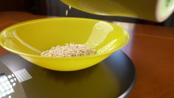 Quelqu'un mesure un morceau de riz brun, sur une balance électronique dans la cuisine. verser la croupe dans un bol rond profond, debout sur une plate-forme de pesage plate. 4k, ralenti, tir de poupée — Video